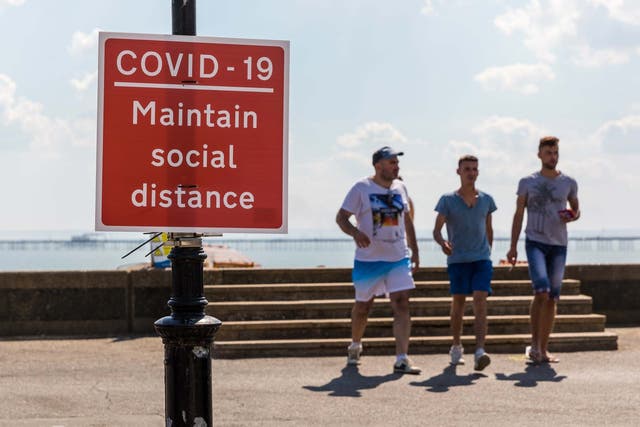 People visiting Southend beach walk past a COVID-19 warning sign to maintain social distance during hot and sunny weather