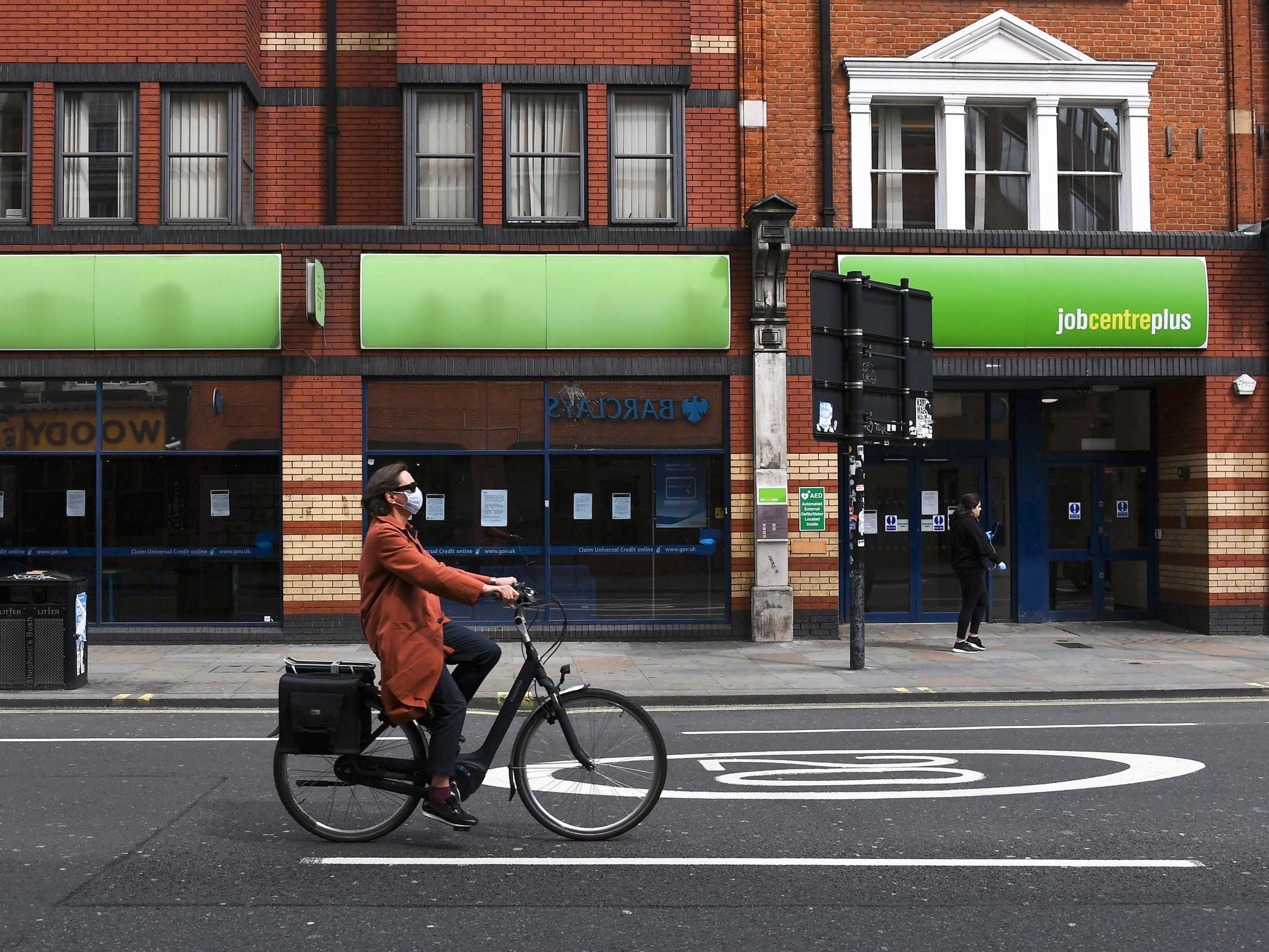 A woman wearing a mask to protect against coronavirus rides a bicycle past a job centre