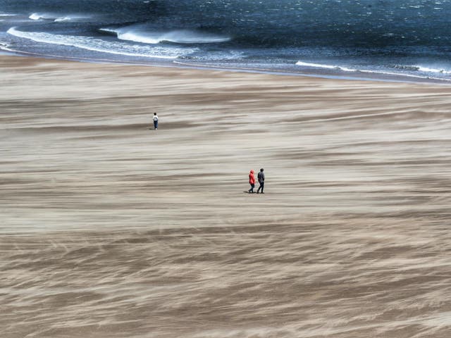Strong winds whip up the sand as people walk along Tynemouth beach on the north east coast