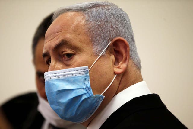 Benjamin Netanyahu, wearing a face mask, looks on while standing inside the court room as his corruption trial opens