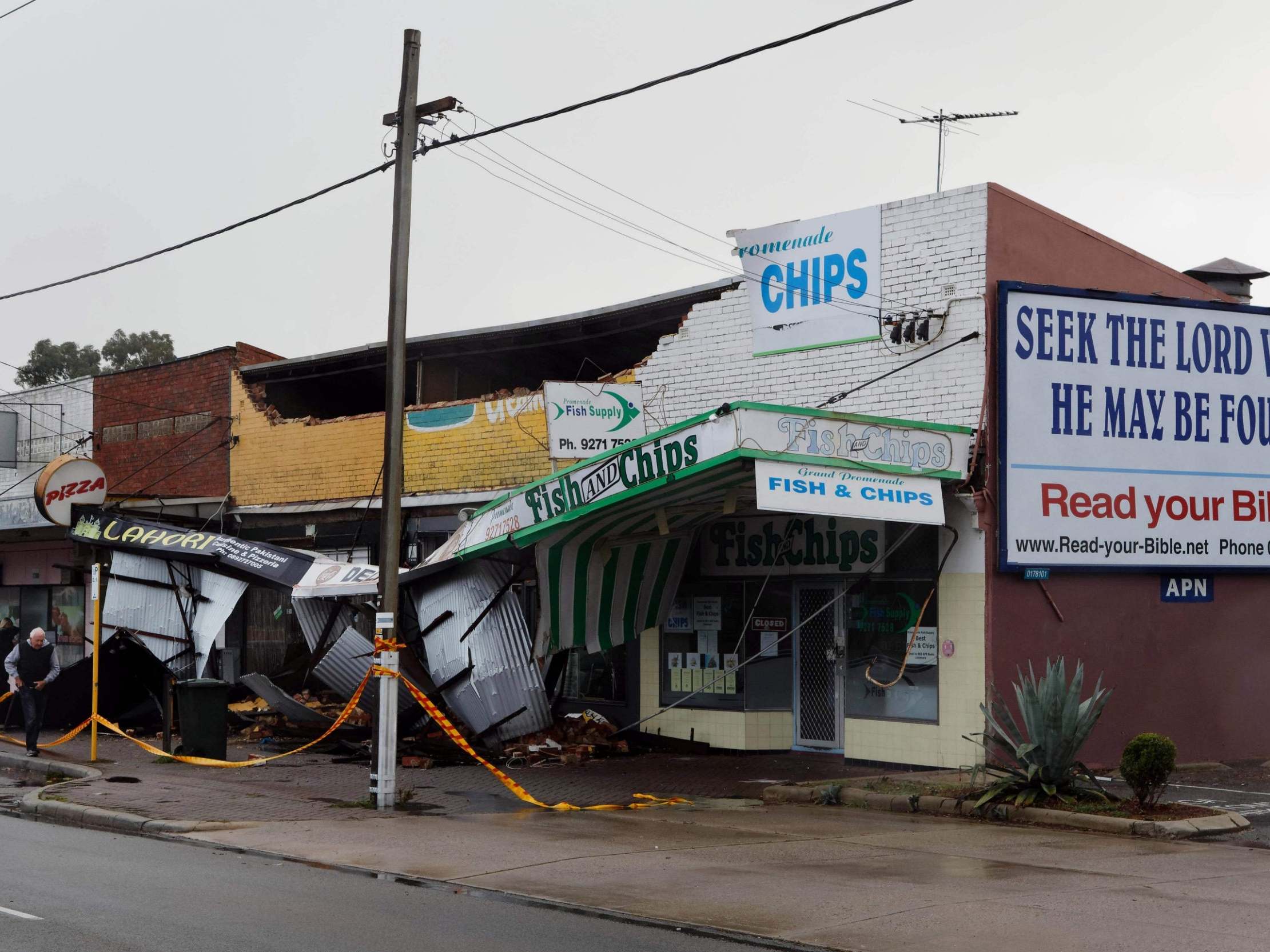 A man (L) walks past shops roped off after they sustained damage in the Perth suburb of Bedford after the area was lashed by gale force winds and a tidal surge from the remnants of Tropical Cyclone Mangga