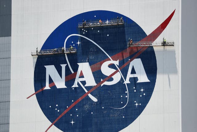 Workers freshen up the paint on the NASA logo on the Vehicle Assembly Building before the arrival of NASA astronauts Bob Behnken and Doug Hurley at the Kennedy Space Center on May 20, 2020 in Cape Canaveral, Florida