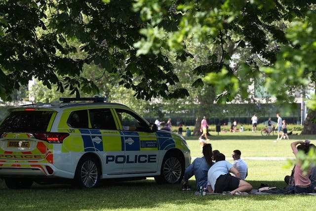 Police officers in a patrol car move sunbathers in Greenwich Park, London