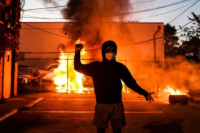 A protestor gestures as cars burn behind him during a demonstration in Minneapolis