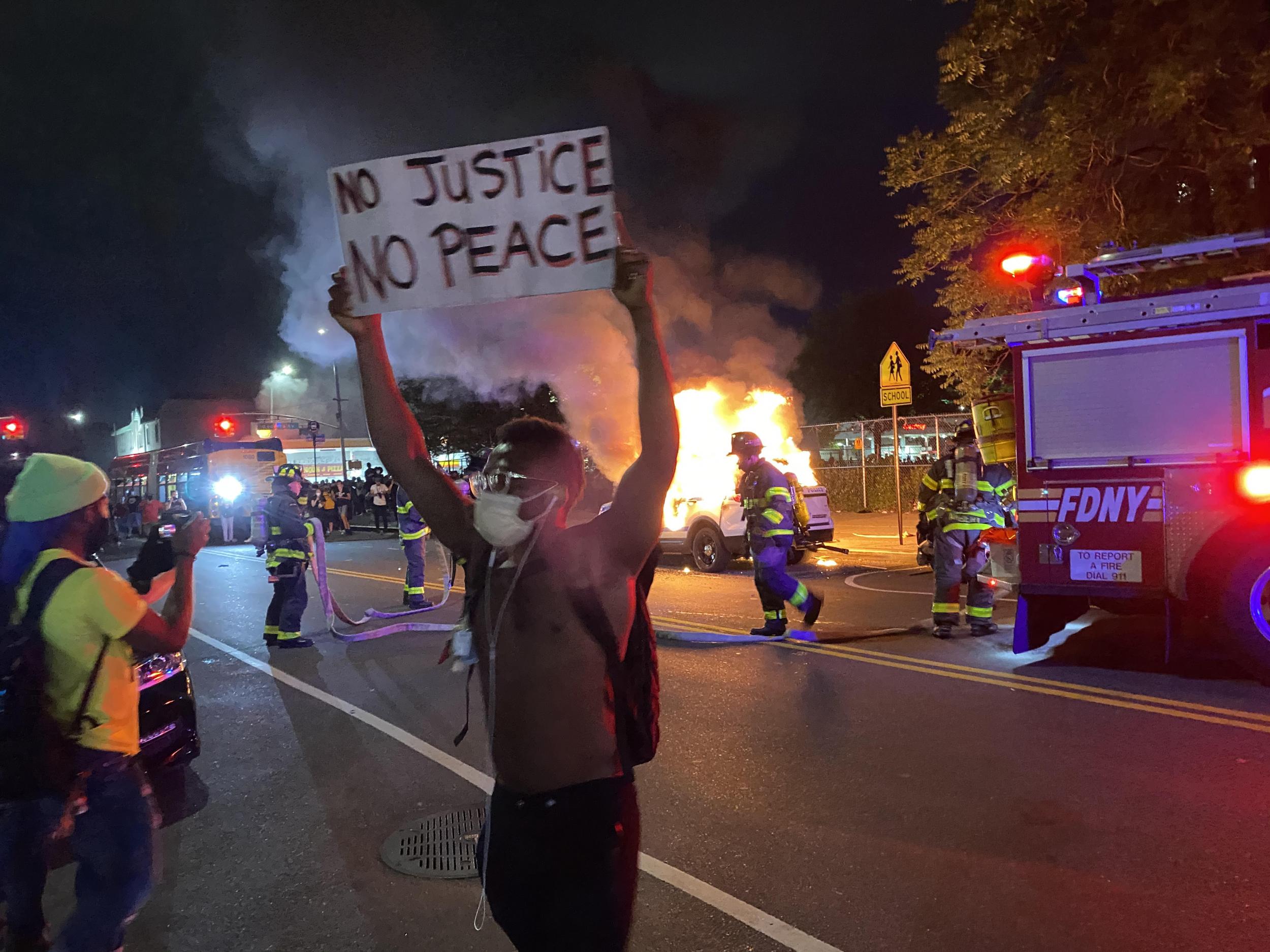 No justice, no peace: a protester stands in front of a burning police car in Brooklyn