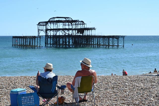 People sunbathe on the beach near the derelict West Pier in Brighton on the south coast of England on May 31, 2020 on the eve of a further relaxation of the novel coronavirus lockdown rules