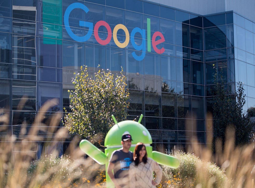 People pose for a picture near a Google sign and Android statue at the Googleplex in Menlo Park, California