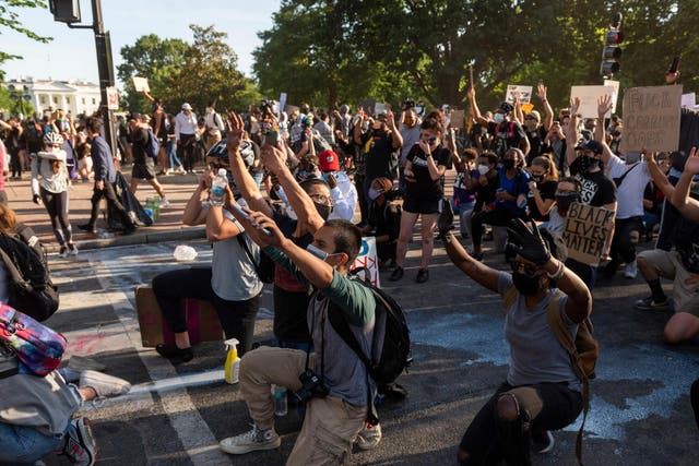 Protestors take a knee and raise their hands as they face riot police near the White House