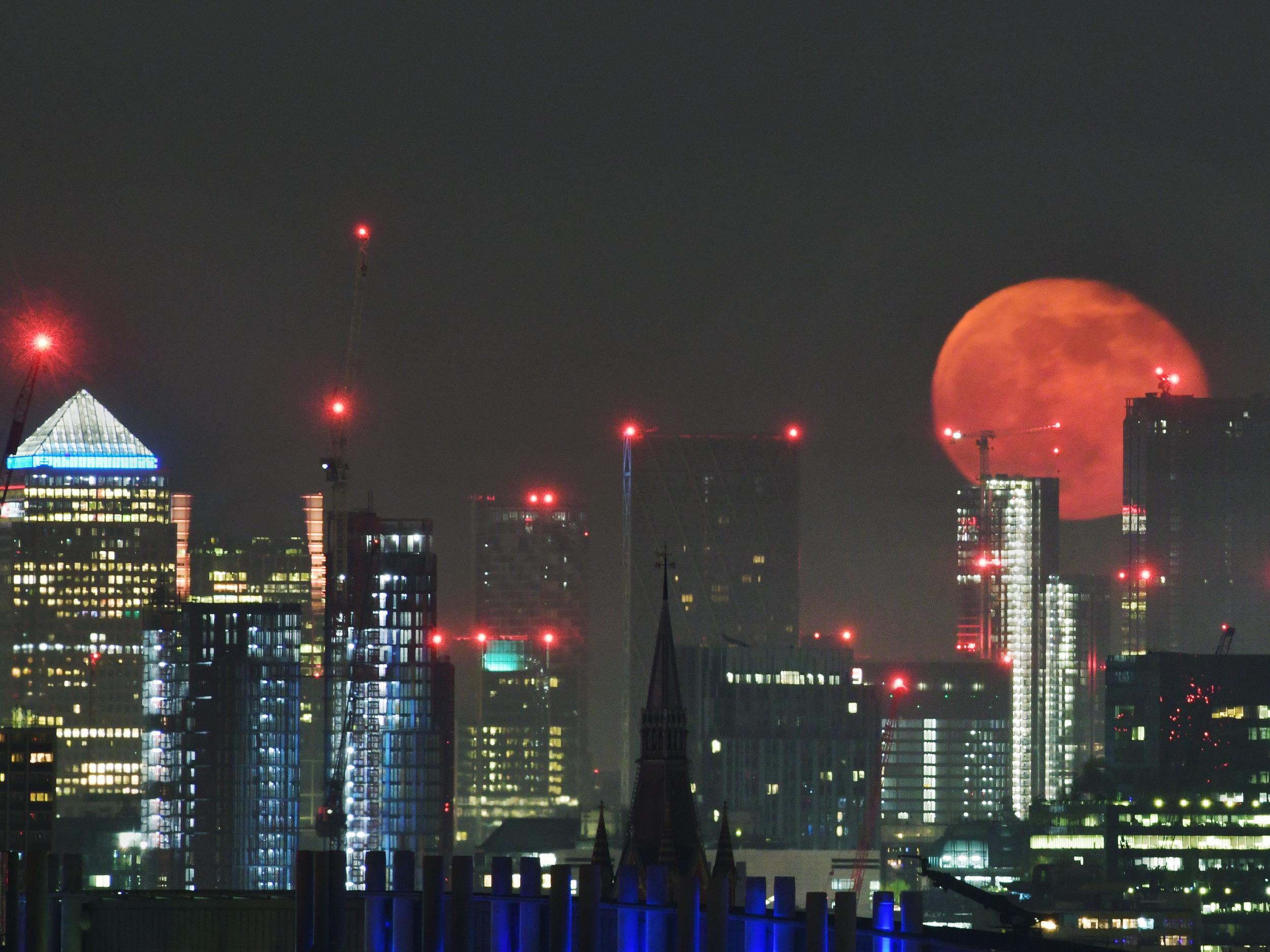 A full moon rising over the sky scrapers of London's Canary Wharf.