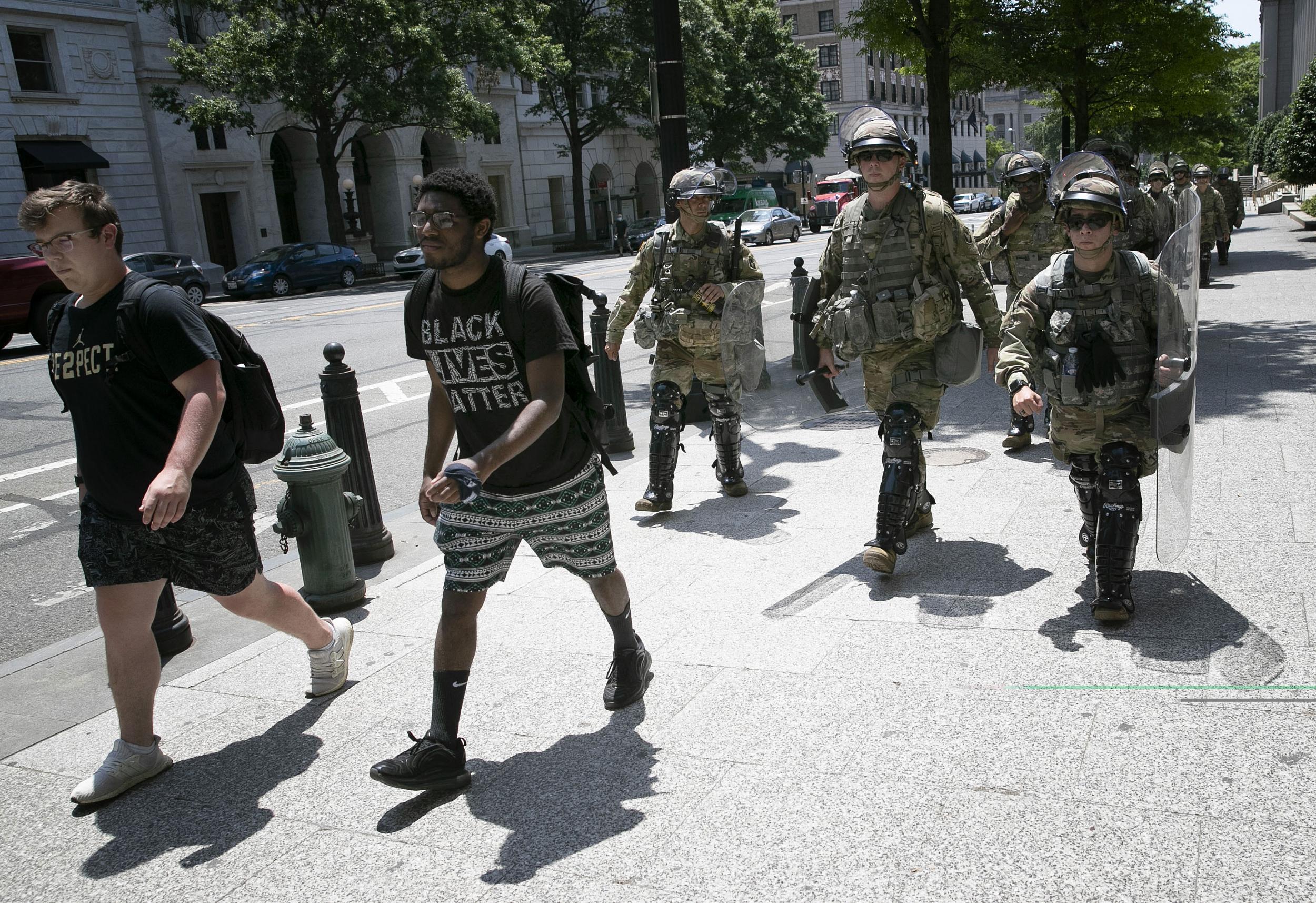 Members of an airborne military unit tasked with crowd control walk behind two protesters outside the US Treasury Building on Thursday