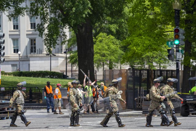 Military personal walk out of the White House as workers build a metal fence reinforced with concrete block on 15th Avenue