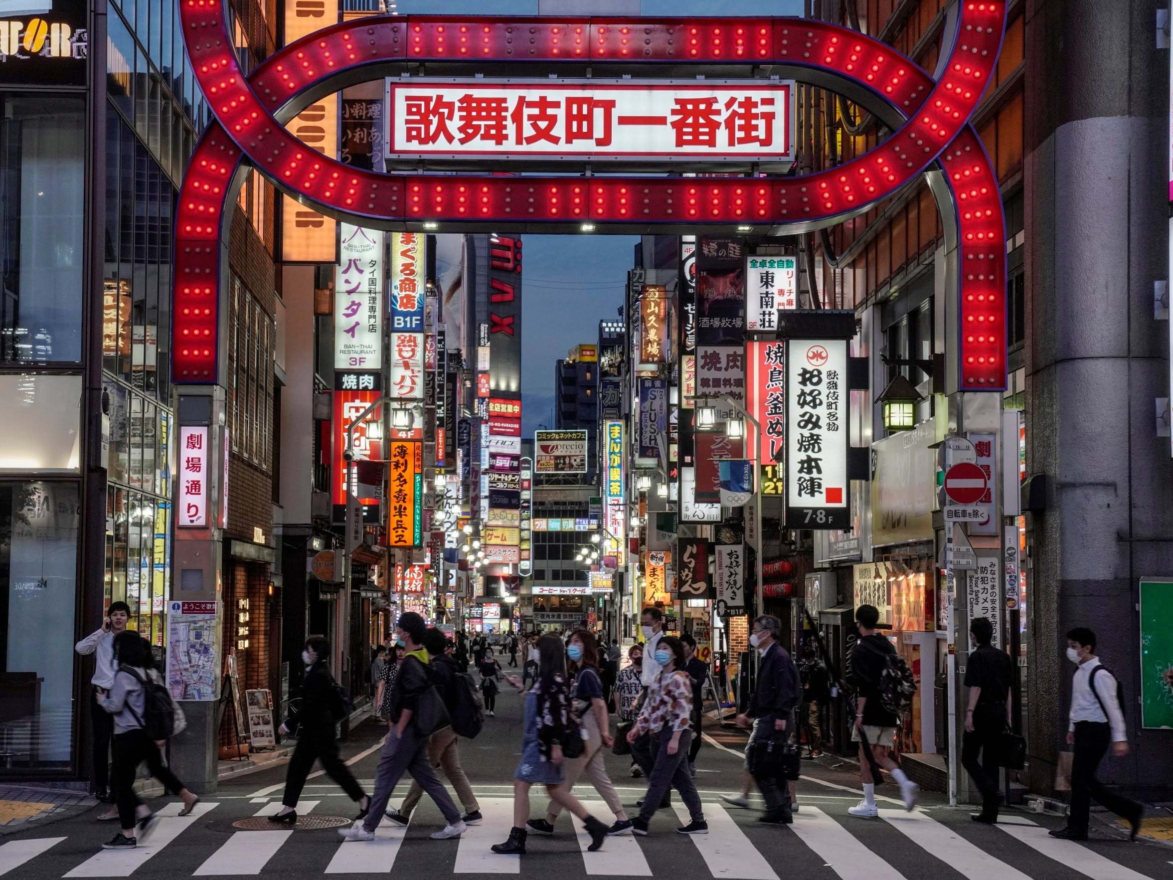 Commuters walk toward a railway station in front of an entrance to Kabukicho, Japan's biggest nightlife entertainment district at Shinjuku, in Tokyo, 25 May 2020.