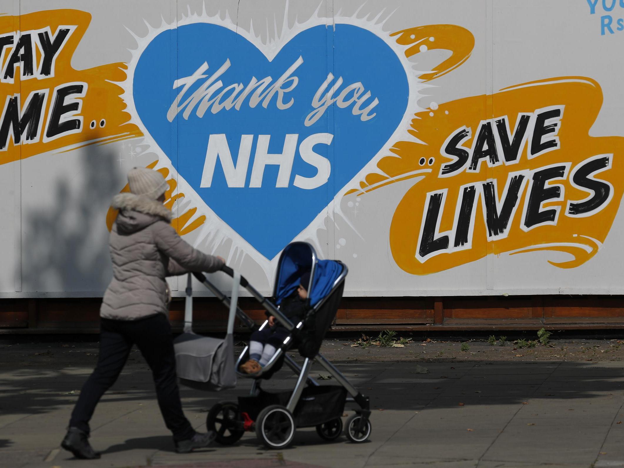 A mother walks past a covered bar with a ‘Thank you NHS’ painting on it in London