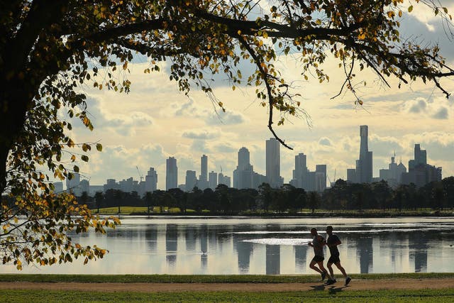 Two joggers run along Albert Park Lake on an Autumn day with high-rise and apartment buildings in the city in the background on June 16, 2017 in Melbourne, Australia
