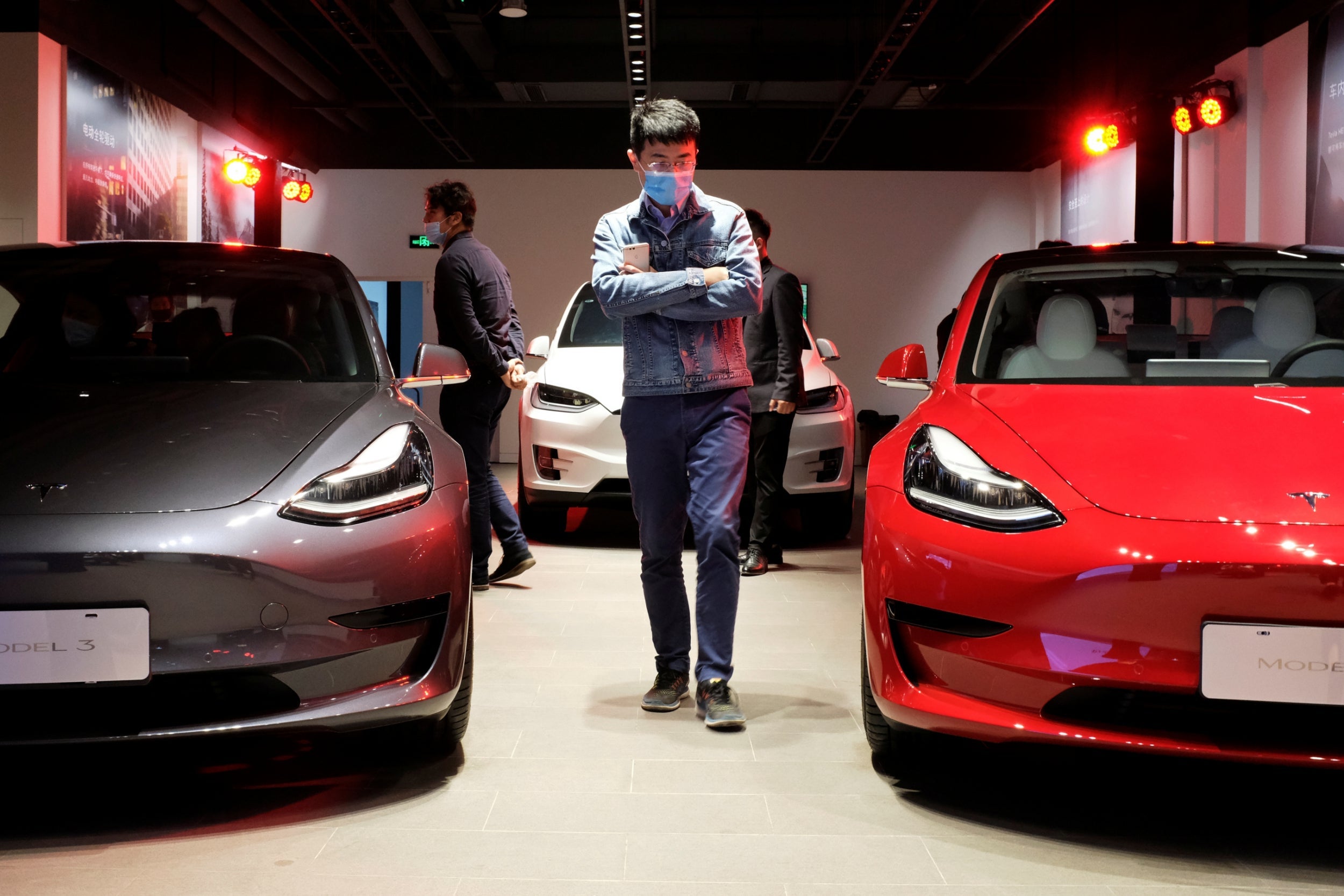 Shoppers in face masks following the coronavirus outbreak view Tesla Model 3 sedans and Tesla Model X sport utility vehicles at a new Tesla showroom in Shanghai, China in May