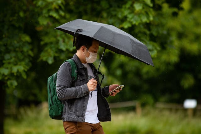 A man wearing a face mask shelters from the rain under an umbrella in London