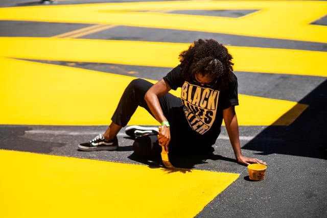 A woman paints a ‘Black Lives Matter’ mural on a street in Brooklyn, New York