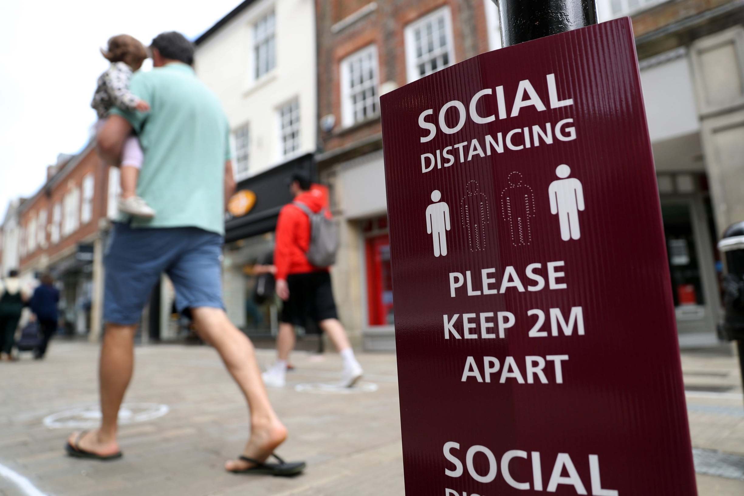 People walk past a social distancing sign on the high street in Winchester as non-essential shops reopened
