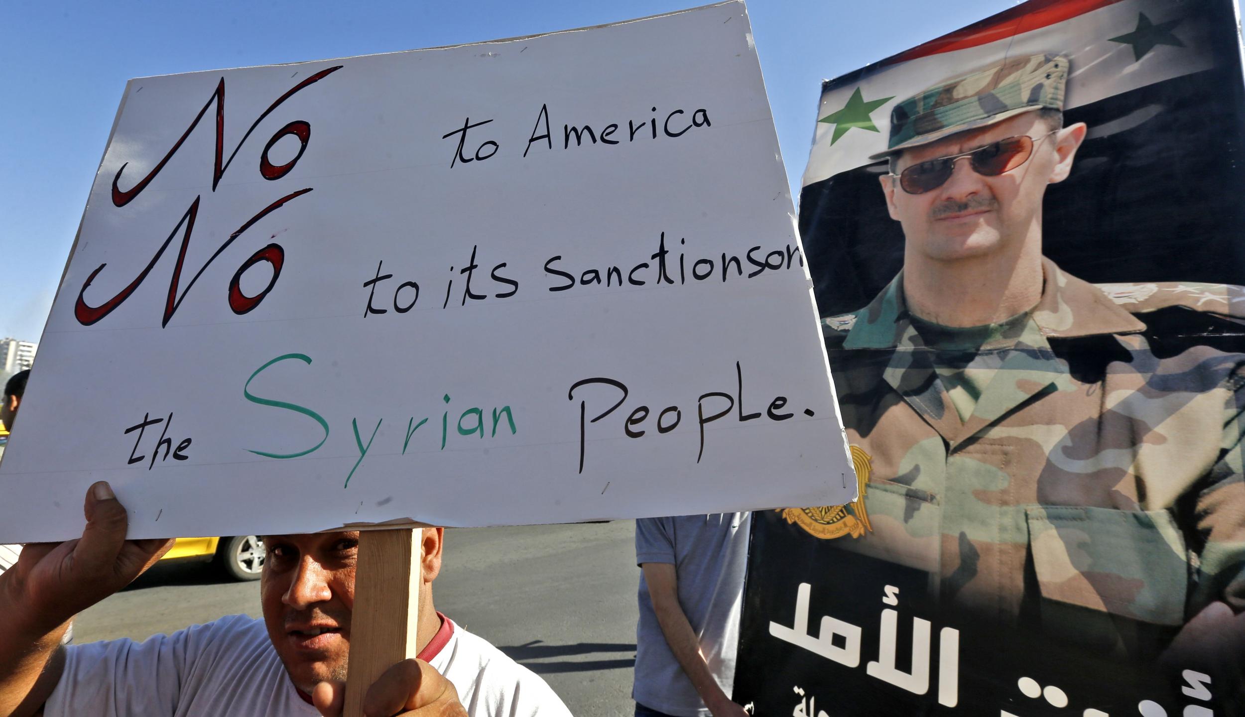 A man holds up a sign as he joins others gathering for a demonstration in support of Syria's President Bashar al-Assad and against US sanctions on the country, in the centre of the capital Damascus