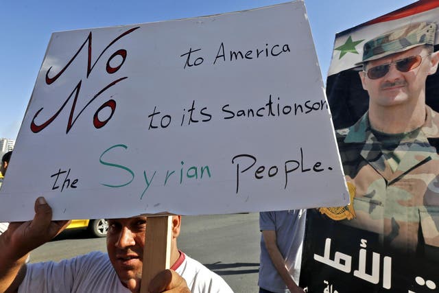 A man holds up a sign as he joins others gathering for a demonstration in support of Syria's President Bashar al-Assad and against US sanctions on the country,  in the centre of the capital Damascus