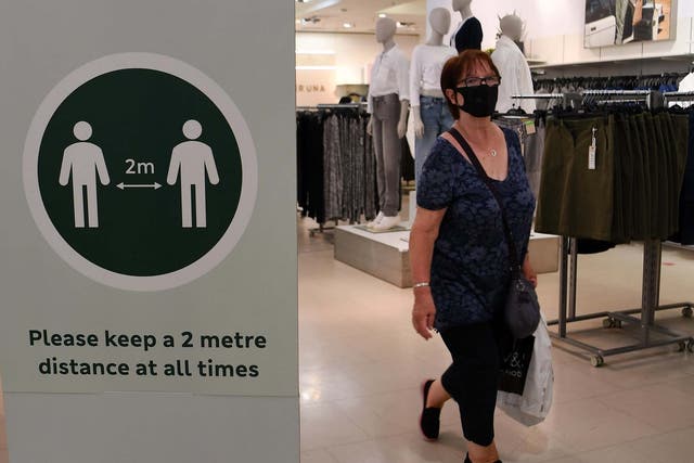 A woman wears a face mask as she walks past a sign reminding customers to keep a minimum distance of 2 meters between each other at a Marks & Spencer store on Oxford Street