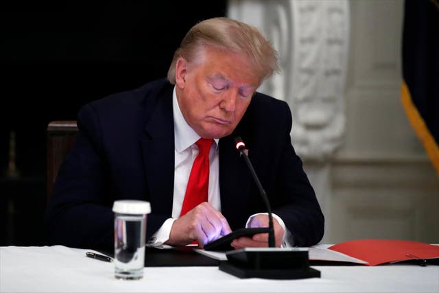 Donald Trump uses his phone during a round table meeting on reopening small businesses hit by the coronavirus pandemic, in the state dining room of the White House