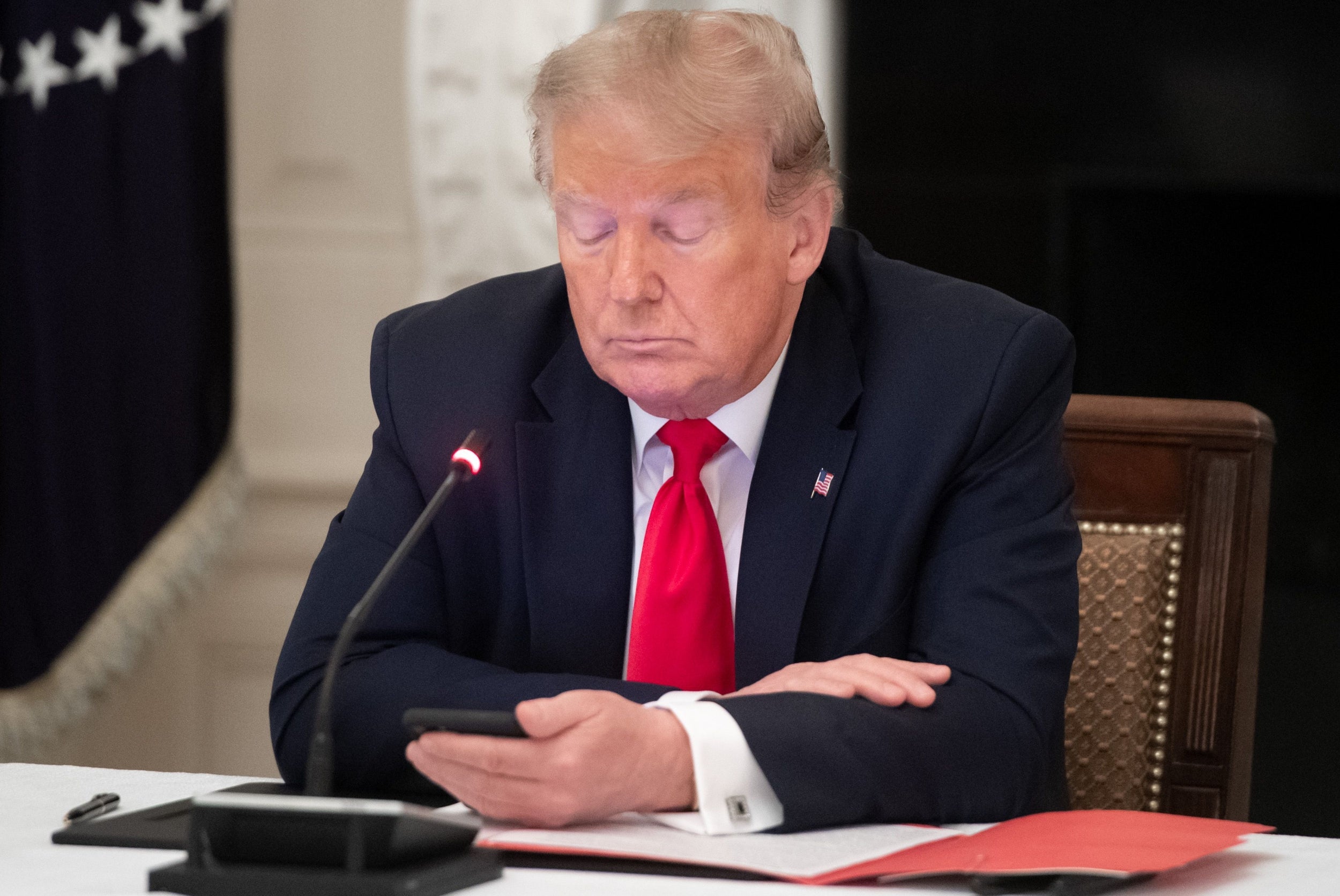 Donald Trump uses his cellphone as he holds a roundtable discussion with governors about the economic reopening of closures due to coronavirus, in the State Dining Room of the White House