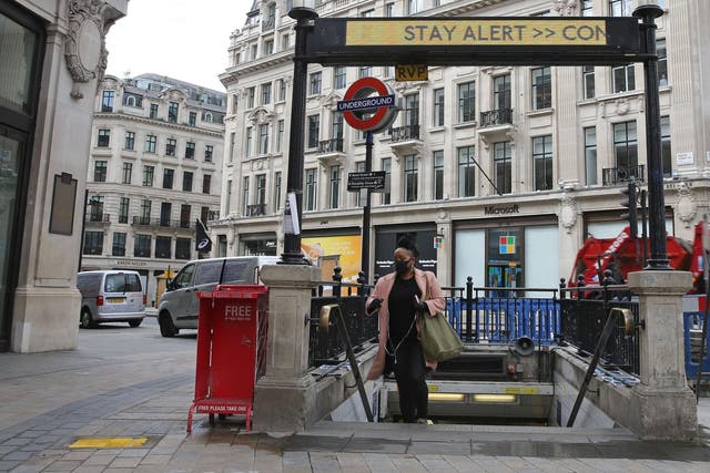 A commuter wearing PPE passes beneath the government's slogan: 'Stay Alert, Control the Virus, Save Lives' above the exit to Oxford Circus Underground station in central London