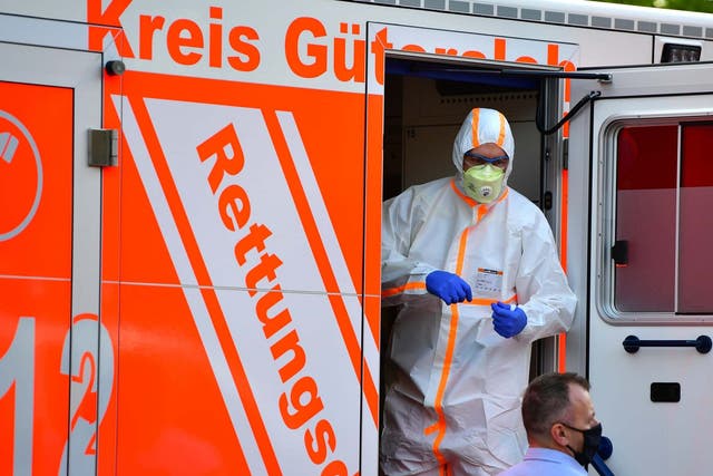 A paramedic wearing full body protection stands inside an ambulance whilce local police forces secure an apartment complex used by the Toennies meat company to house foreign workers from eastern Europe during the coronavirus pandemic