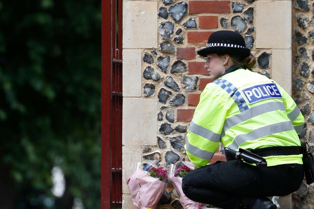 A police officer collects flowers left at the Abbey gateway of Forbury Gardens, Reading, following a multiple stabbing attack