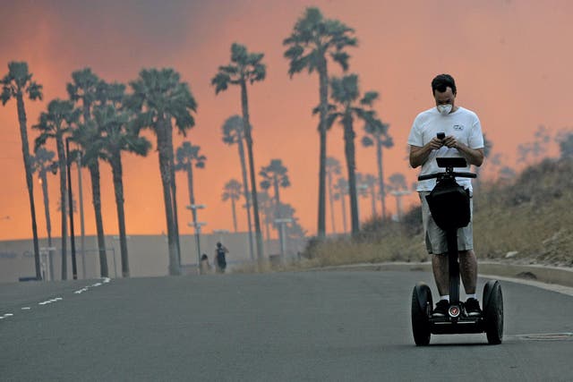 A man uses his cell phone while riding a Segway November 15, 2008 as the glow from a fire is seen in the distance in Yorba Linda, California