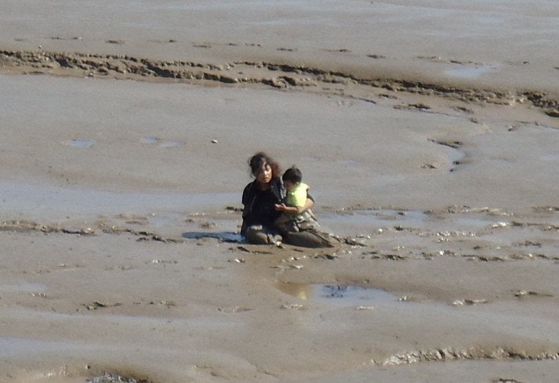 A woman attempts to carry a small child back to the shore