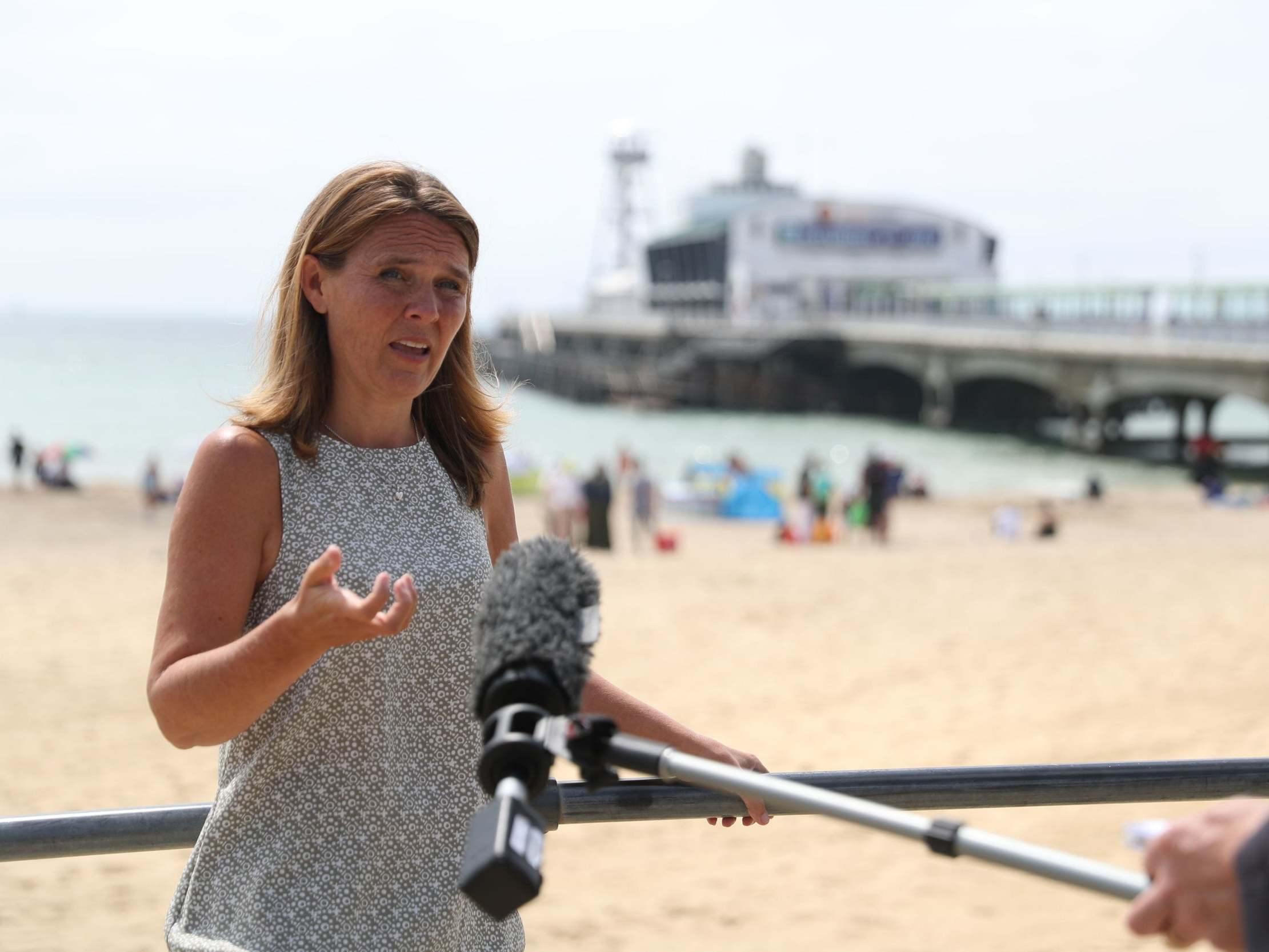 Vikki Slade, leader of Bournemouth, Christchurch and Poole Council, gives a video interview as people relax on the beach near Bournemouth Pier where three men were stabbed, 26 June 2020.