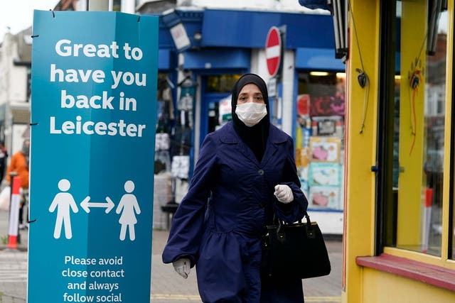 A woman wearing a PPE mask walks past social distance advisory signs in Leicester's North Evington neighbourhood on June 29, 2020 in Leicester, England.