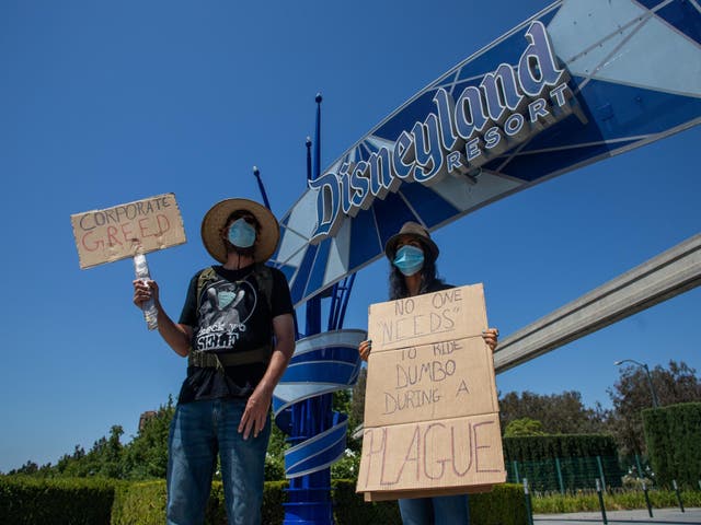 People hold signs in front of Disneyland in California calling for higher safety standards before its reopening on 17 July, amid the coronavirus pandemic in Anaheim