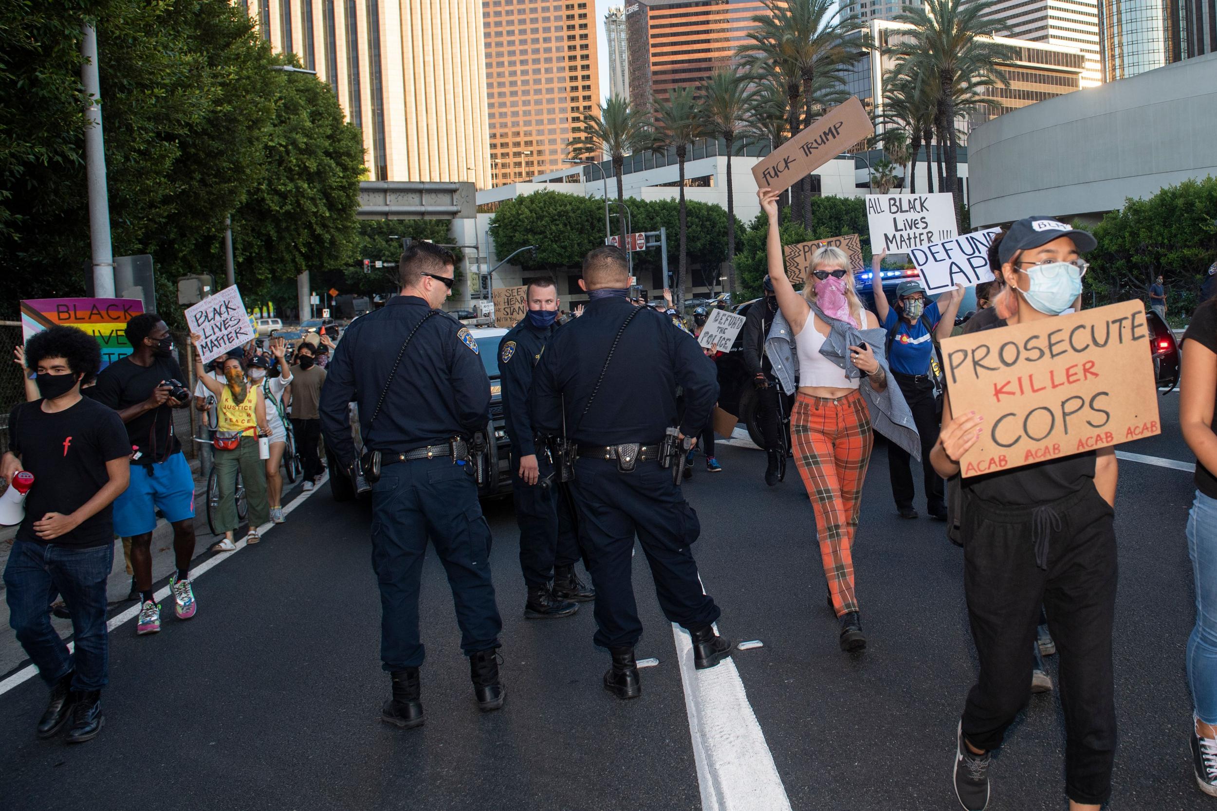 Protesters walk past police officers as they march toward the freeway during a demonstration calling for the removal of DA Jackie Lacey and to defund the police on 1 July