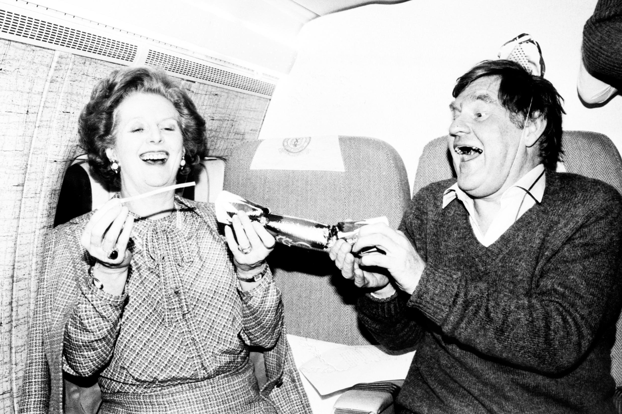 Prime minister Margaret Thatcher pulls a Christmas cracker with her chief press officer Bernard Ingham during a flight from Washington to London in 1984