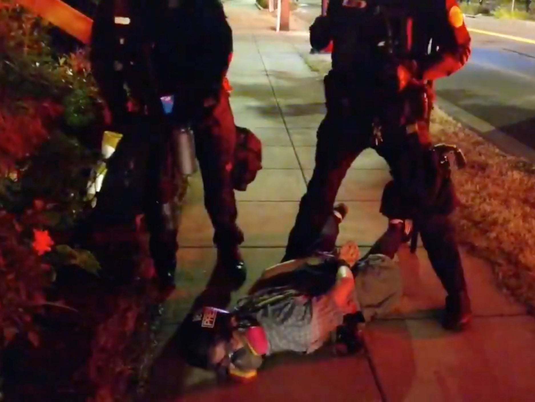Journalist Justin Yau lies handcuffed on the ground with police officers standing over him at a demonstration in Portland, Oregon