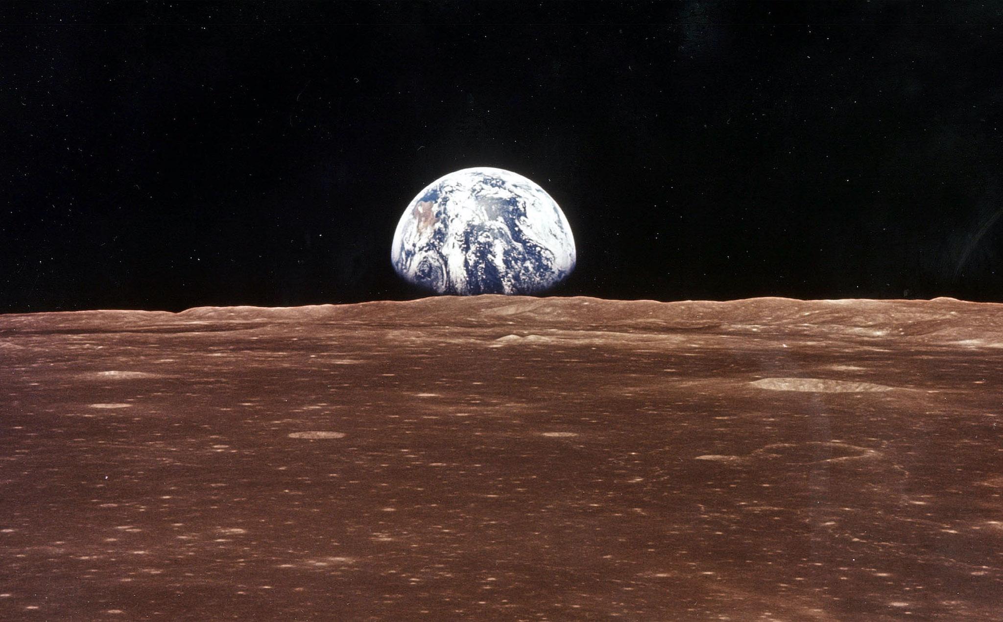 A view of the Earth appears over the Lunar horizon as the Apollo 11 Command Module comes into view of the Moon