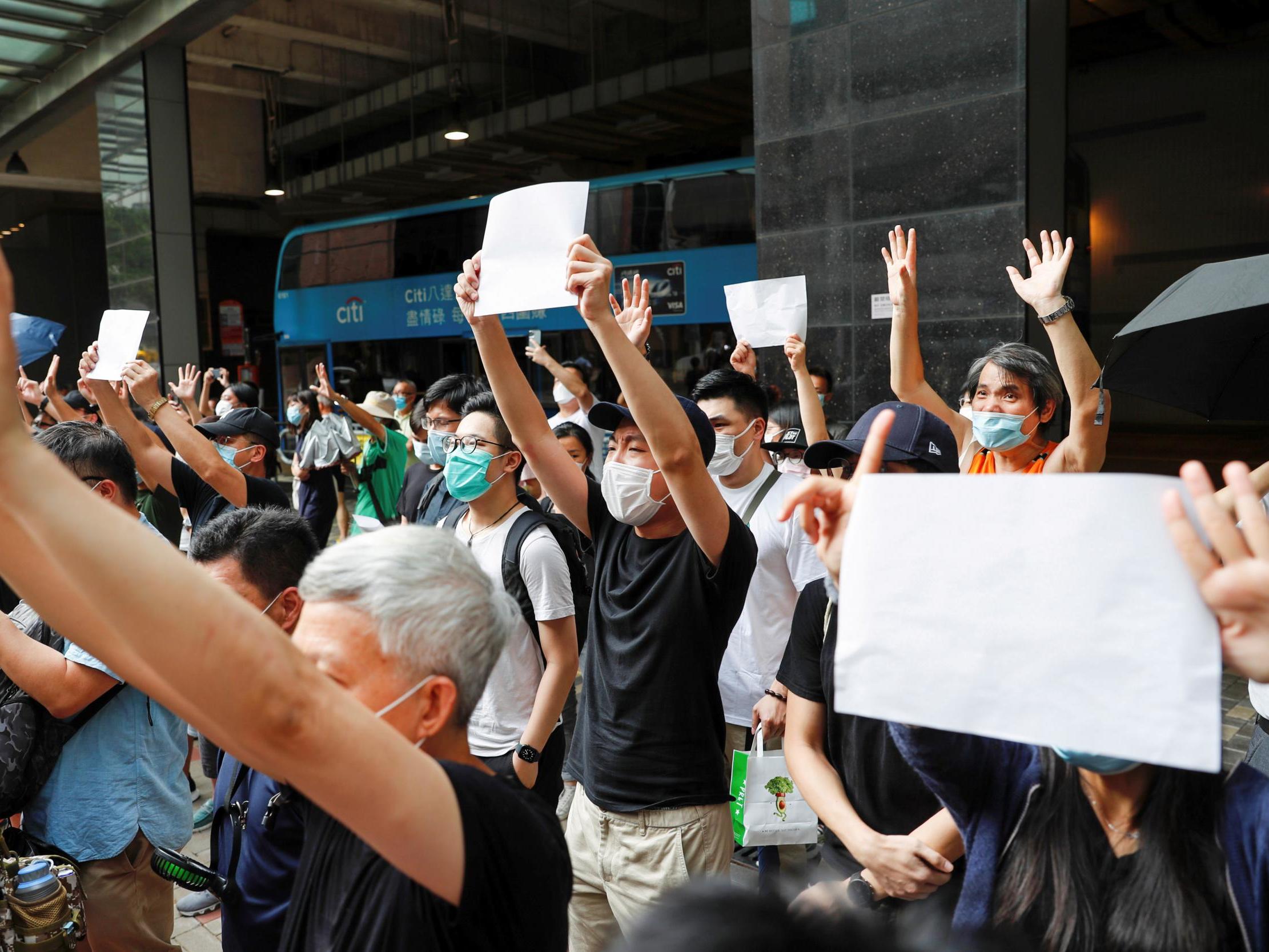 Supporters of an arrested anti-law protester raise white paper to avoid slogans banned under the national security law