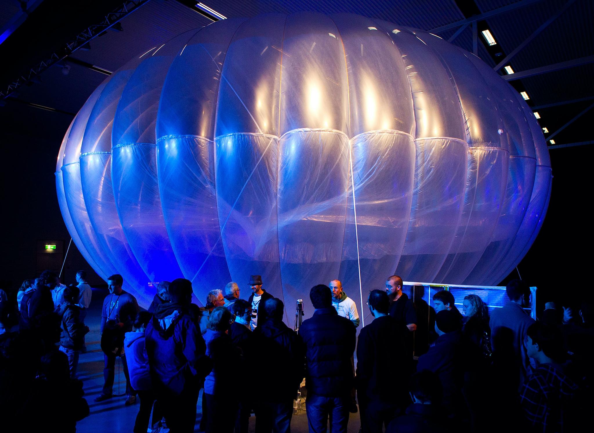 Visitors stand next to a high altitude WiFi internet hub, a Google Project Loon balloon, on display at the Airforce Museum in Christchurch on June 16, 2013