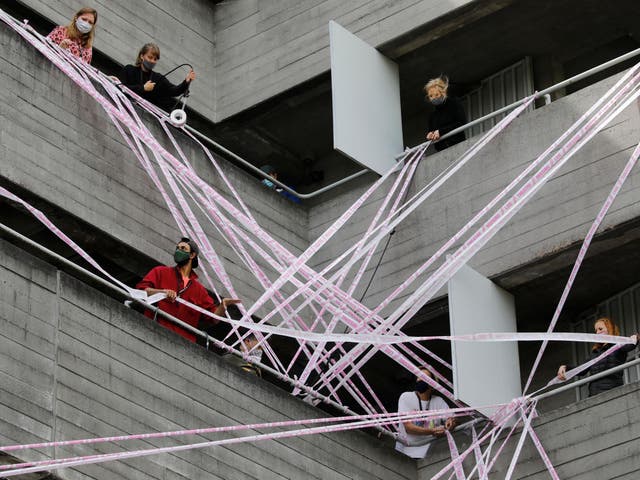 Volunteers from the #MissingLiveTheatre initiative wrap pink tape reading "missing live theatre" on the National Theatre, 3 July, 2020