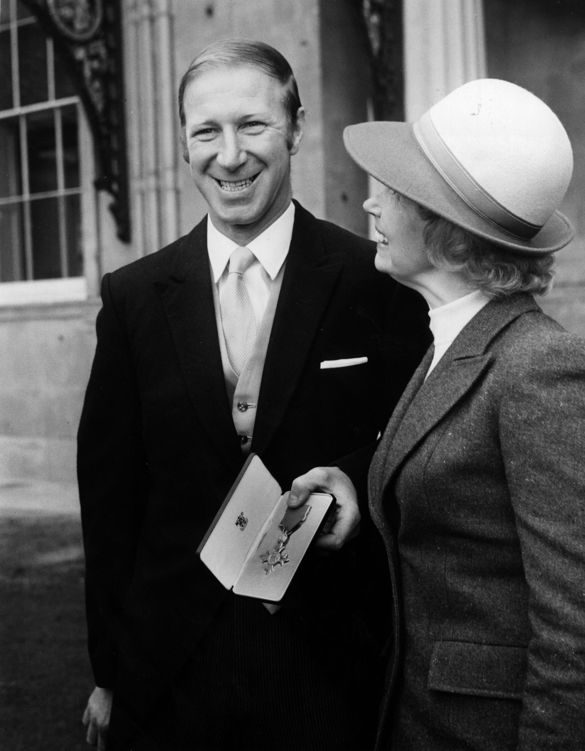 Charlton, with his wife Pat, displays his OBE outside Buckingham Palace in 1974