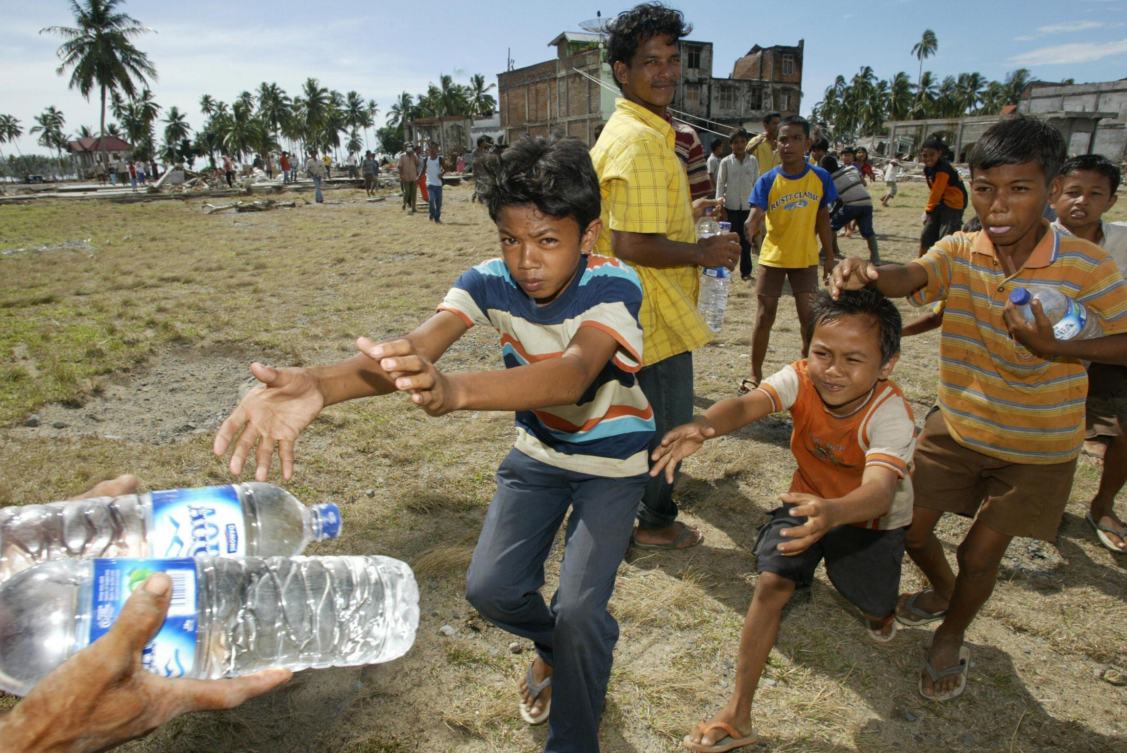 Children run for bottles of water brought by US aid workers to the hard-hit village of Teunom, on the west coast of Aceh province