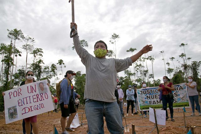 Un familiar de una víctima de COVID-19 sostiene una pala junto a otro familiar quien levanta un cartel que dice "Por un entierro digno".