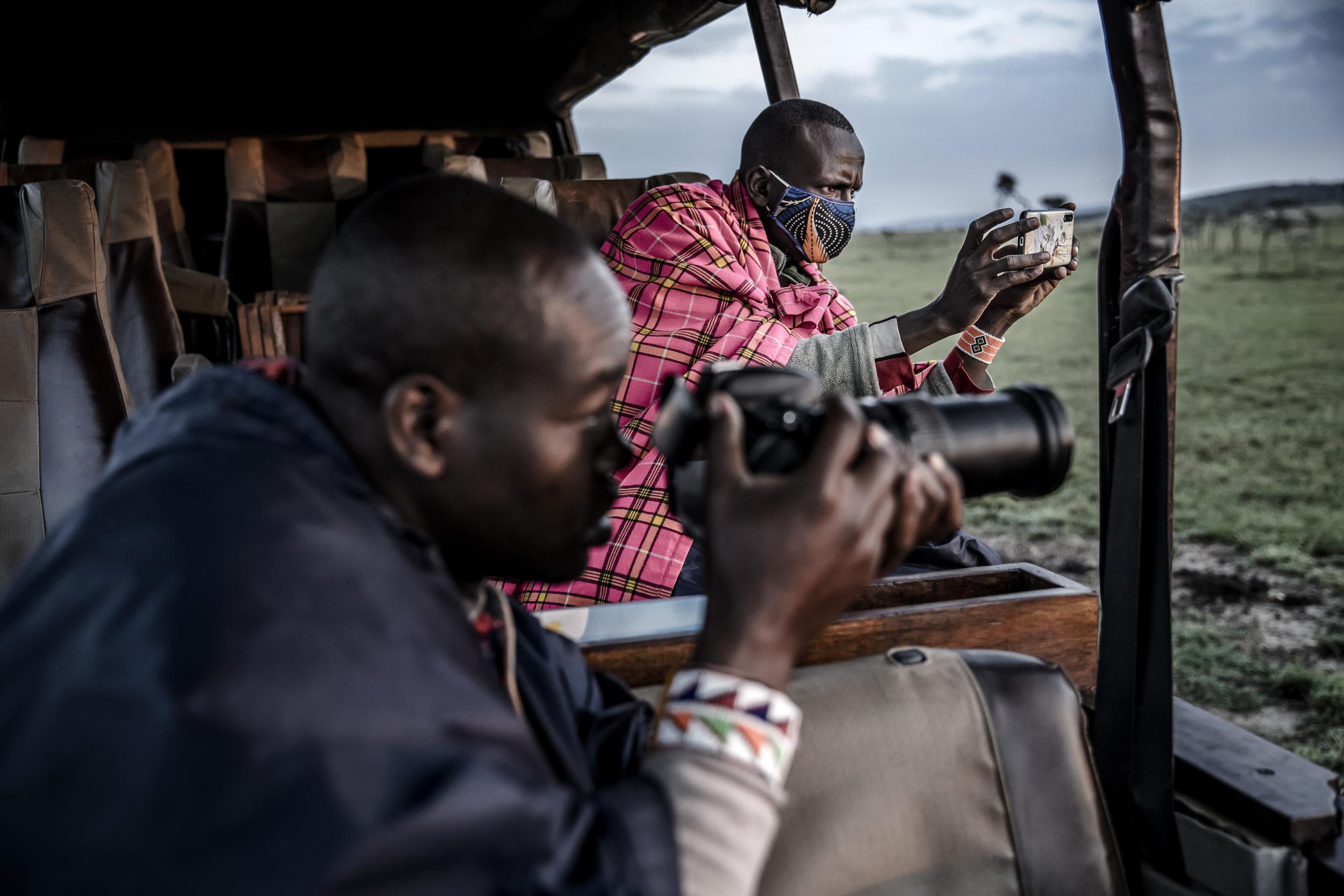 Ben Tongoyo, a Maasai safari guide working with Ol Kinyei Conservancy, takes pictures and videos of a lion with his phone for a virtual safari