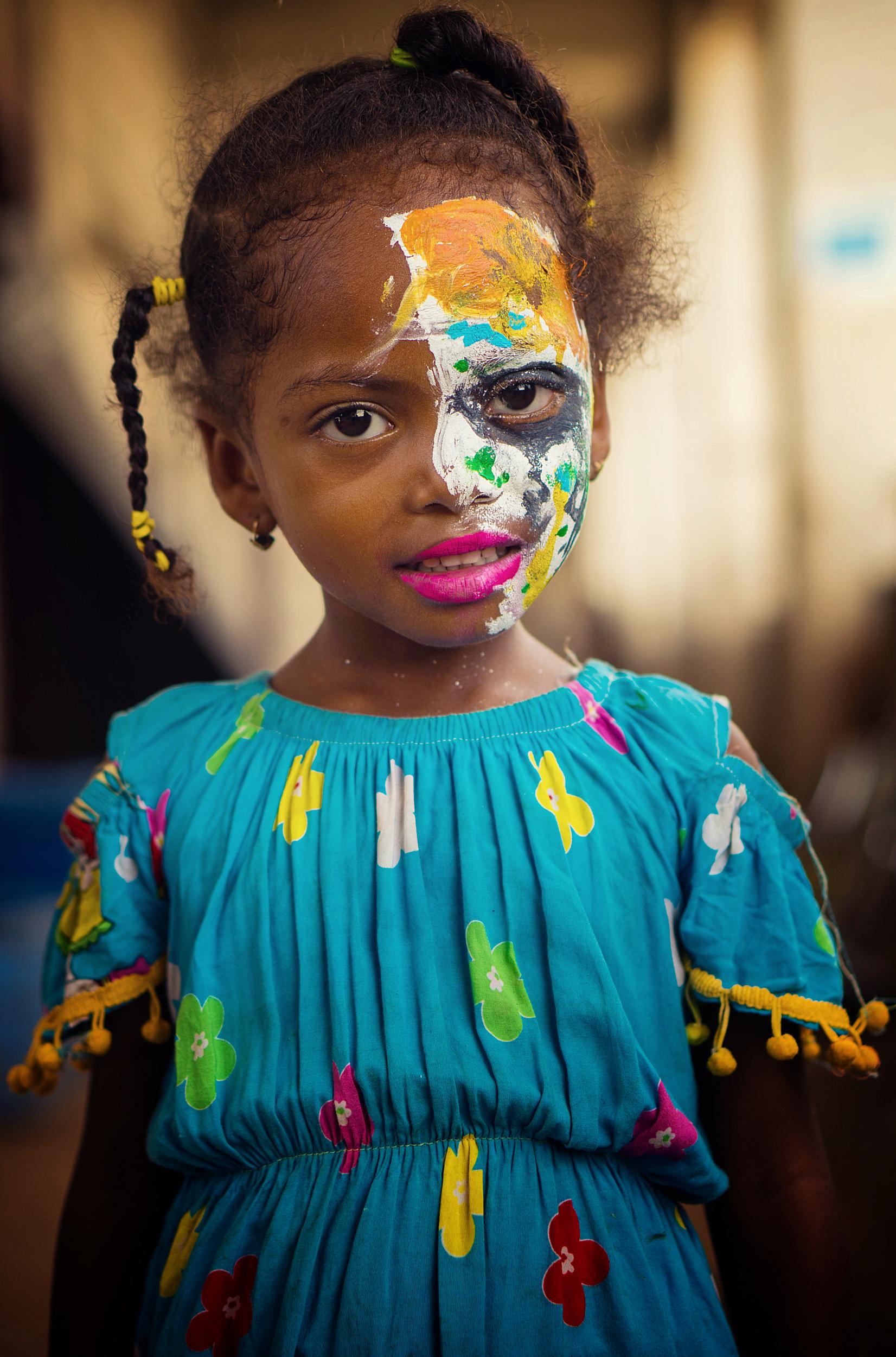 A four-year-old girl poses for a picture in a camp for internally displaced people in Yemen. She came to this camp with her family after fleeing the war in their home in Al-Hodaieda governorate. She has a friend in the camp who loves face-painting the other children. With no schooling available to them, the children find creative ways to pass their time and make small amounts of money where they can