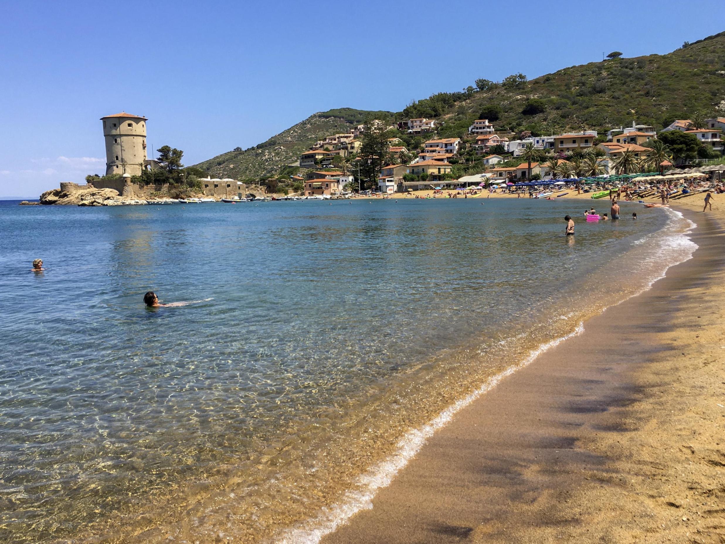 People enjoy the sun and the fresh water on a beach at the Giglio island, in front of Tuscany, Italy