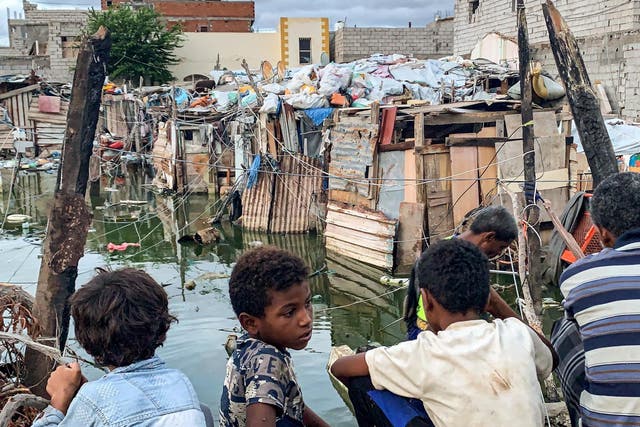 Children watch as workers prepare to drain sewage water from an Aden camp flooded by rainwater for Yemenis displaced by conflict from Taez, Ibb, and Hodeidah