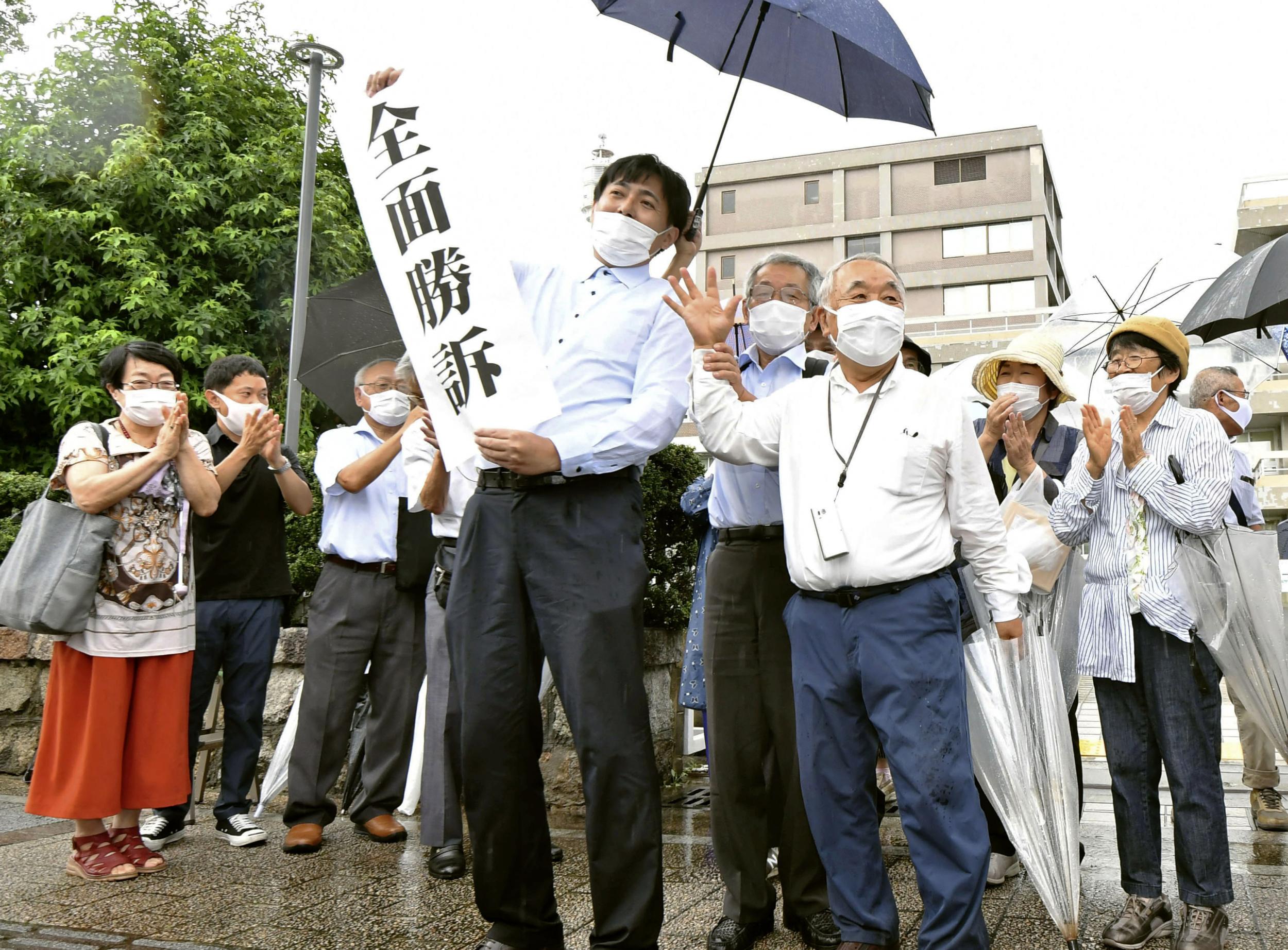 A group of supporters for plaintiffs celebrate, holding a banner which reads ‘Overall victory’ outside the Hiroshima district court